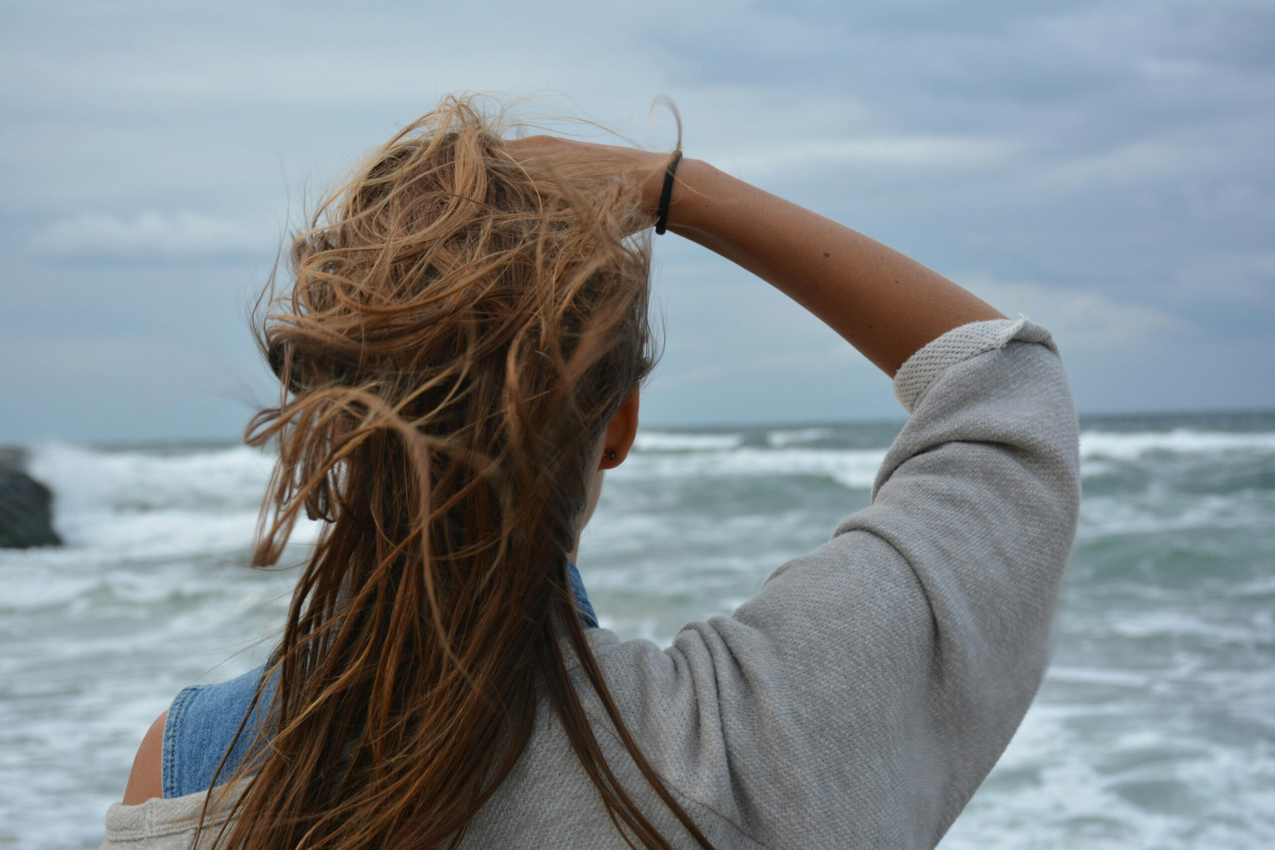 Back view of a young woman with tousled hair observing a windy ocean seascape.